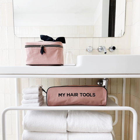 Bag-all Medium Box Makeup & Toiletry case in blush pink with black bow and striped lining, shown with matching hair tools case on modern white bathroom counter with towels