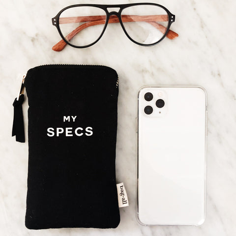 Bag-all My Specs Glasses Case in black canvas with white text, shown with aviator glasses and smartphone, featuring exterior pocket and tassel zipper pull on marble surface