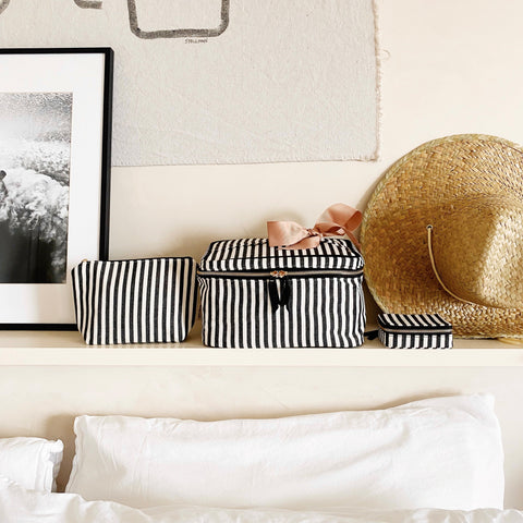 Bag-all Cutest Striped Travel Gift Set 3-Pack featuring black and white striped cotton makeup bag, toiletry case, and pill organizer displayed on white shelf with straw hat and framed artwork
