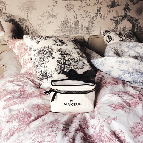 Bag-all My Makeup Cosmetic Box in cream white with black text, displayed on pink and white toile bedding, featuring zipper closure and practical design for beauty storage and organization