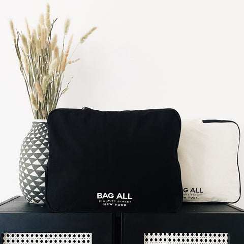 Bag-all Large Double Sided Packing Cube in Black with logo, displayed beside geometric vase with dried pampas grass, minimalist travel organization solution