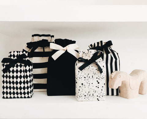 Bag-all Gift Bag Splatter Small with black and white geometric patterns, stripes, and paint splatter designs, adorned with elegant ribbon bows, displayed alongside matching reusable fabric gift bags