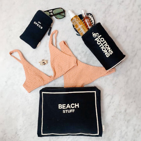 Bag-all Stylish Beach Essential Set in black featuring waterproof pouches for sunglasses, lotions, and beach items, displayed with coral bikini and beach accessories on marble surface