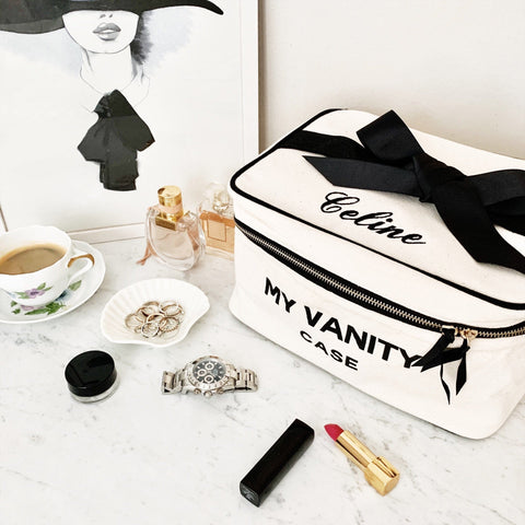 Bag-all My Vanity Large Beauty Box in cream with elegant black bow, displayed on marble surface with makeup, jewelry, and perfume, perfect for organizing cosmetics and travel