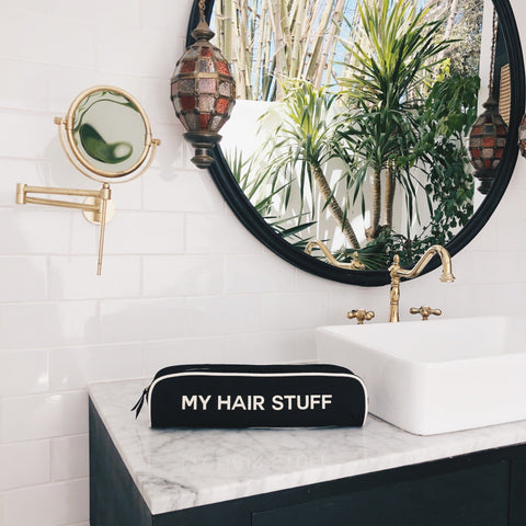 Bag-all Hair Stuff Travel Case in black displayed on marble bathroom counter, featuring stylish organization for heat styling tools and accessories against modern decor with round mirror
