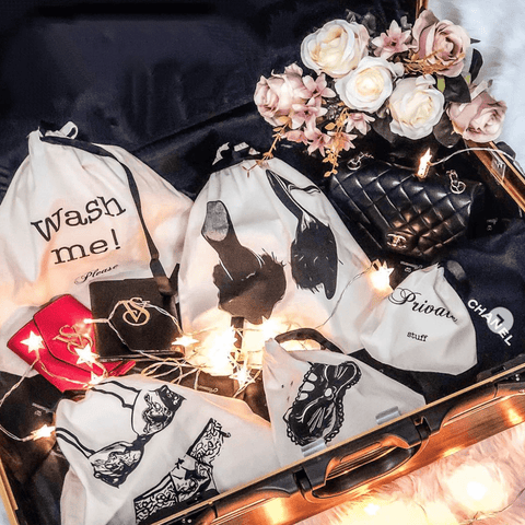 Bag-all Feather Slippers Shoe Bag in cream shown with stylish collection of travel organizer bags, decorated with string lights and elegant roses, displayed on dark silk fabric