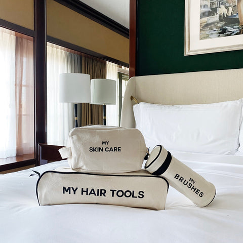 Bag-all Pamper Gift Set Deal 3-Pack Cream featuring natural cotton organizers for hair tools, brushes, and skincare, displayed on crisp white hotel bedding with elegant table lamps