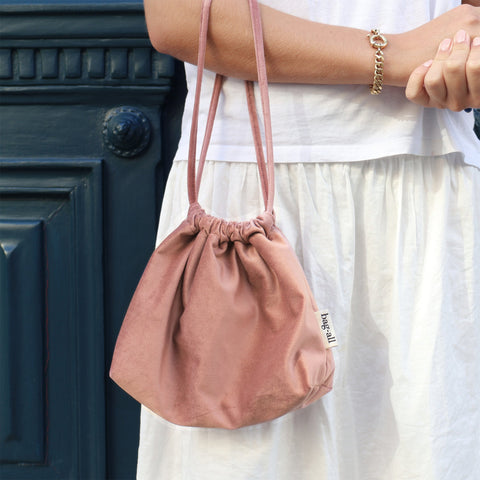 Pink velvet drawstring tech pouch by Bag-all held by person in white dress outdoors for stylish storage