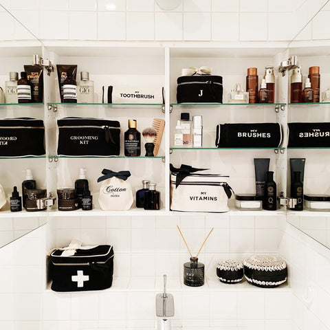 Bag-all Vitamins Storage and Travel Box in cream color displayed in an organized bathroom shelf alongside other black and white toiletry cases and grooming essentials for stylish bathroom organization