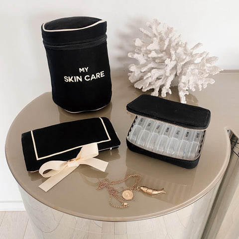 Bag-all Essential Gift Set 3-Pack in Black featuring skincare case, pill organizer, and jewelry roll pouch, displayed on gray surface with decorative coral accent