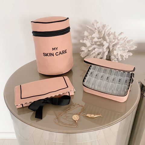 Bag-all Essential Gift Set 3-Pack in pink featuring skincare case, pill organizer, and jewelry roll pouch, displayed on gray surface with decorative coral accent