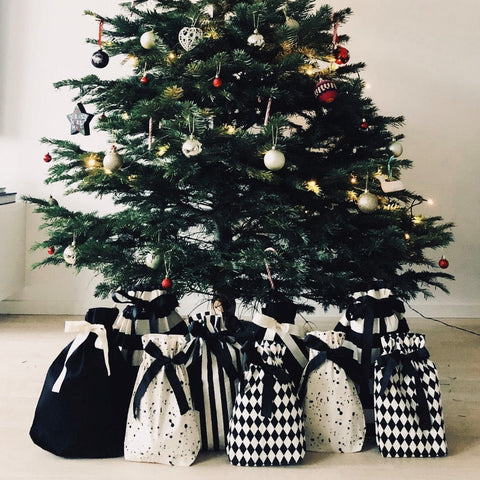 Bag-all Gift Bag Striped Large collection showcased under Christmas tree, featuring black and white patterned reusable fabric bags with geometric prints, stripes, and dots, arranged elegantly around tree base