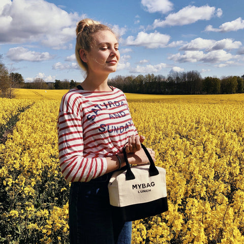 Bag-all Lunch Box Insulated in Cream shown in vibrant yellow rapeseed field, featuring black and cream design, insulated material for temperature control, compact size with comfortable handle