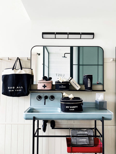 Bag-all Pink First Aid Storage Box with black cross print and bow, shown with other organizing cases on vintage-style bathroom vanity, featuring eco-friendly cotton material