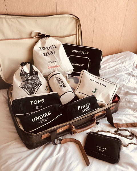 Bag-all cream Wash Me Laundry Bag shown with coordinating travel organizer bags in suitcase, featuring tops, undies, and toiletry compartments in black and cream cotton canvas