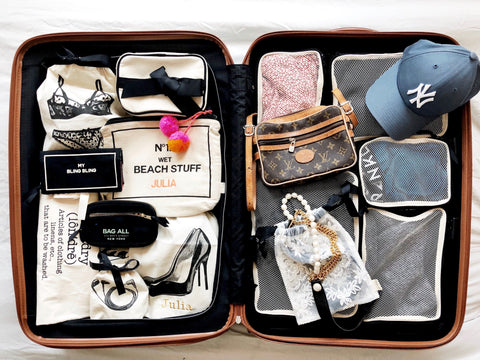 Bag-all Cotton Packing Cubes in black shown organizing travel items in open suitcase, featuring mesh compartments with various clothing, accessories, and beach essentials neatly arranged