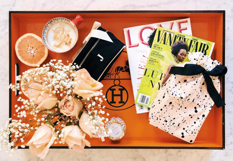 Bag-all Gift Card displayed on orange tray with peach roses, coffee cups, fashion magazines, grapefruit, and Hermes box, creating a luxurious lifestyle setting