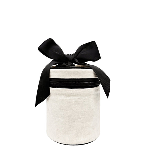 Cream round carry on liquids case with black zipper and large black fabric bow on white background