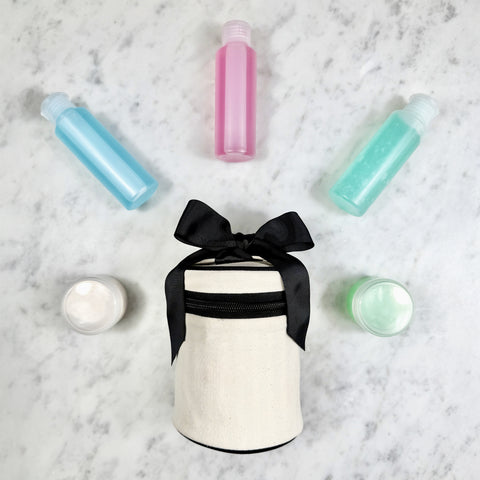 Cream round carry on liquids case with black ribbon and refillable travel bottles and jars on marble surface