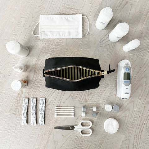 Bag-all First Aid Organizing Pouch in black with striped interior lining, shown with medical supplies including thermometer, mask, and cotton swabs arranged on light wooden surface