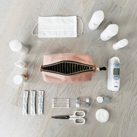 Bag-all First Aid Organizing Pouch in blush pink shown with medical essentials, face mask, thermometer, cotton swabs, scissors and medicine bottles arranged on gray wooden surface