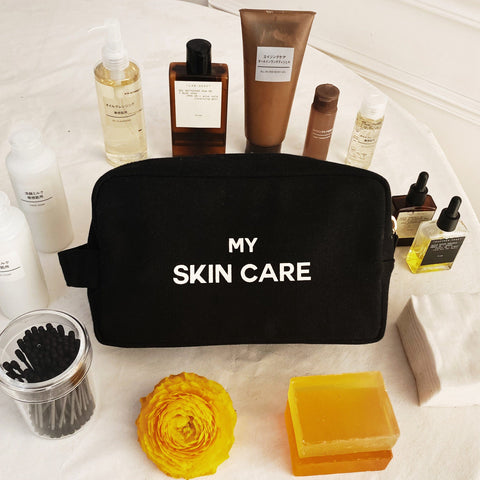 Bag-all My Skin Care black organizing pouch with waterproof lining, gold zipper displayed with skincare products, yellow flower and soap accessories