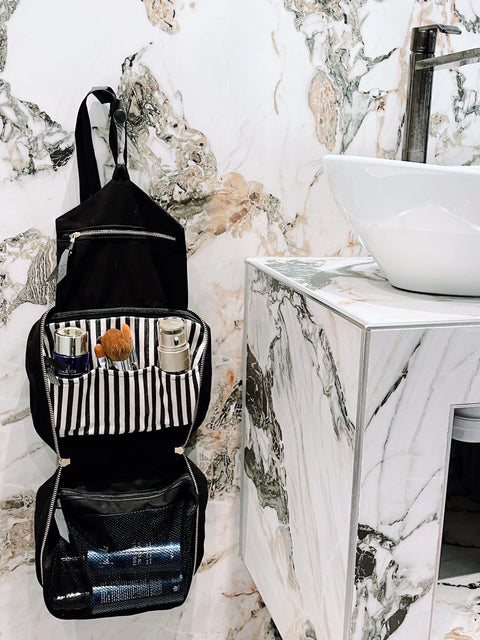 Bag-all Folding/Hanging Toiletry Case in black cotton with striped interior compartments, shown open against marble bathroom counter, perfect for organized travel storage