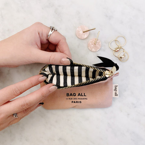 Bag-all Mini Trinket Pouch in pink/blush with black and white striped interior, featuring metal zipper and Paris address. Cotton canvas pouch shown opened displaying organized jewelry storage and rings.