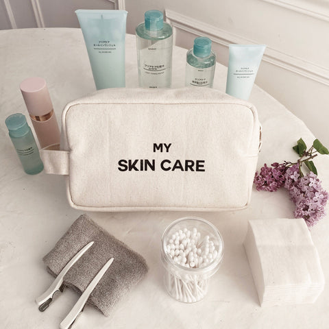 Bag-all My Skin Care Organizing Pouch in natural cotton canvas with waterproof lining, styled with beauty products and lilac flowers on white marble surface