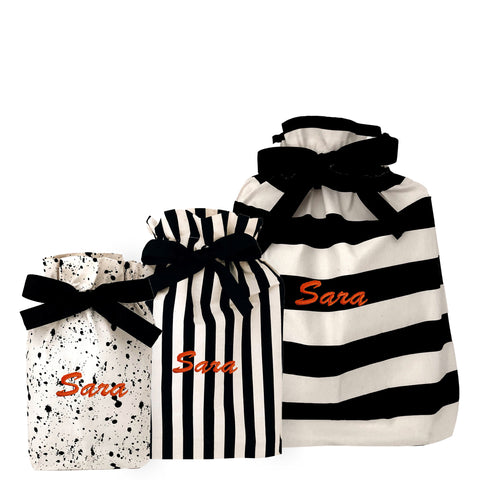 Set of three reusable fabric gift bags in black and white patterns with personalized name Sara in orange.
