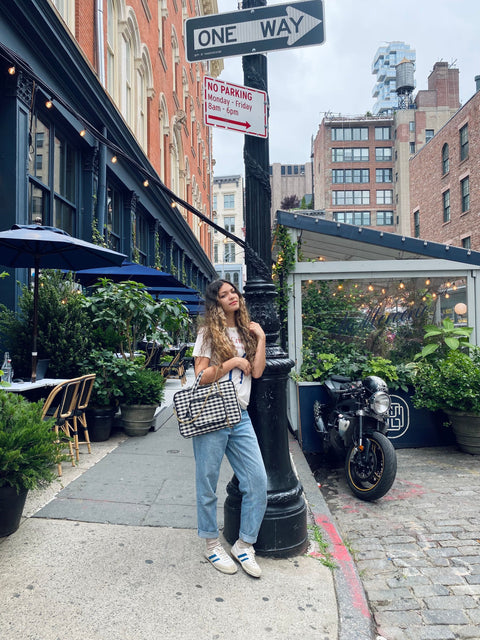 Bag-all Laptop Case 13" in stylish gingham pattern shown on NYC street corner with greenery and urban architecture, featuring handle and charger pocket for convenient carrying and storage.