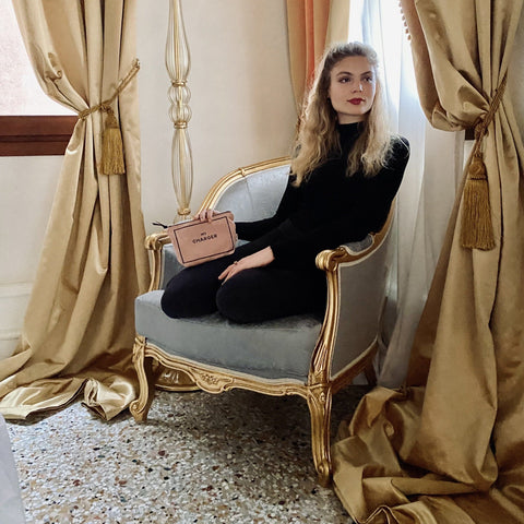 Bag-all Charger Pouch in blush pink displayed on elegant vintage chair, featuring gold zipper, natural cotton material, shown in luxurious setting with cream curtains and ornate furniture