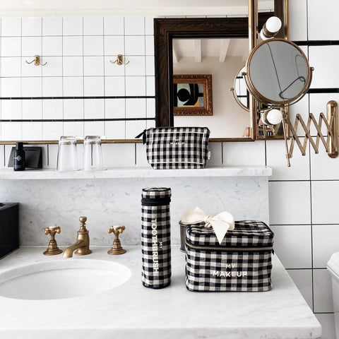 Bag-all My Makeup Pouch in classic black and white gingham pattern with coated lining, displayed on marble bathroom counter with matching gingham accessories and vintage-style brass fixtures