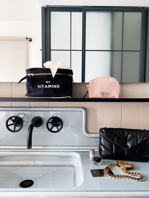 Bag-all Vitamins Storage and Travel Box in black displayed on bathroom counter alongside pink makeup case, showcasing stylish organization for daily supplements