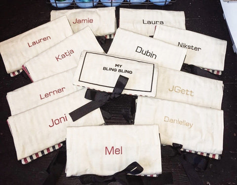 Bag-all Jewelry Organizer Travel Pouches in cream with personalized monogram names, featuring black bows and striped trim, arranged in a circular display pattern