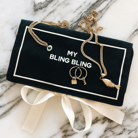 Bag-all black travel jewelry organizer pouch with 'My Bling Bling' text, featuring gold chain necklace and rings displayed on marble surface, white ribbon detail