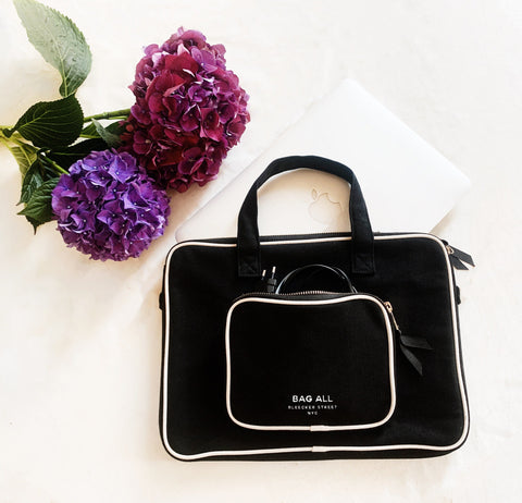 Bag-all Laptop Case 13" in black cotton with double handle, front charger pocket, and white trim detail, styled with purple hydrangea flowers on white surface