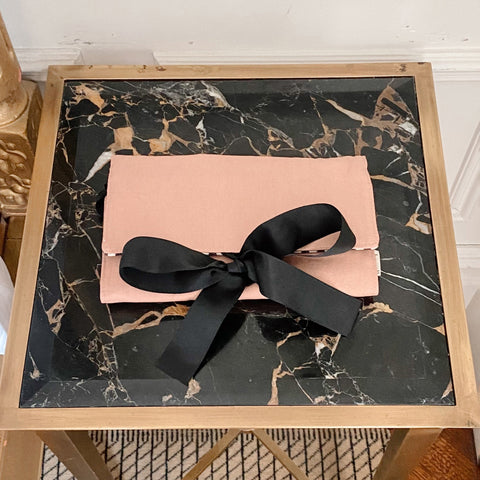 Bag-all Large Jewelry Roll in pink blush with black ribbon bow, perfect for organizing jewelry while traveling, displayed on marble surface in elegant presentation style
