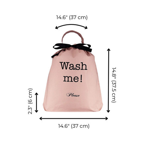 Bag-all pink laundry bag with 'Wash me!' text in black, featuring black bow handle and measurements displayed. Stylish organizer for travel and home use.