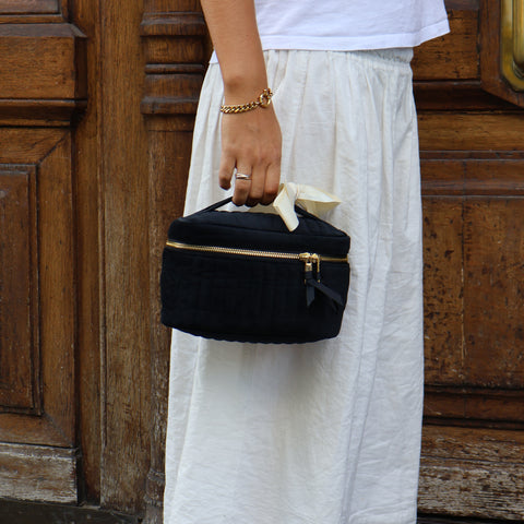 Woman holding a personalized quilted black velvet makeup cosmetic box with gold zipper and cream ribbon handle.