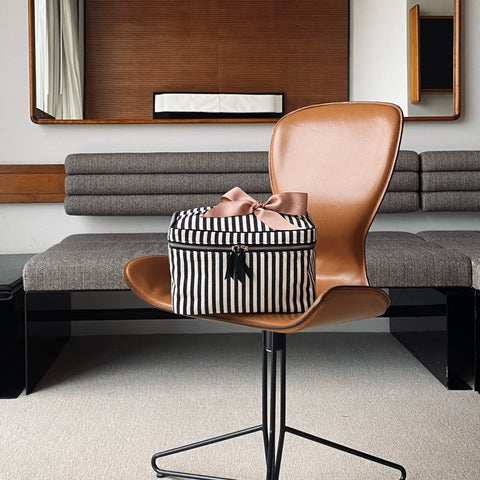 Bag-all Medium Box Makeup & Toiletry in classic black and white stripes with rose gold bow, displayed on modern leather chair, featuring stylish design and convenient storage for beauty essentials