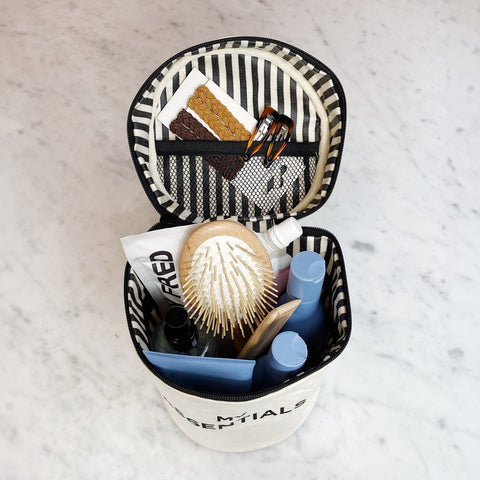 Bag-all Roomy Travel Essentials Case in cream with striped interior, displaying organized toiletries, hairbrush, and cosmetics in cylindrical design with protective lining