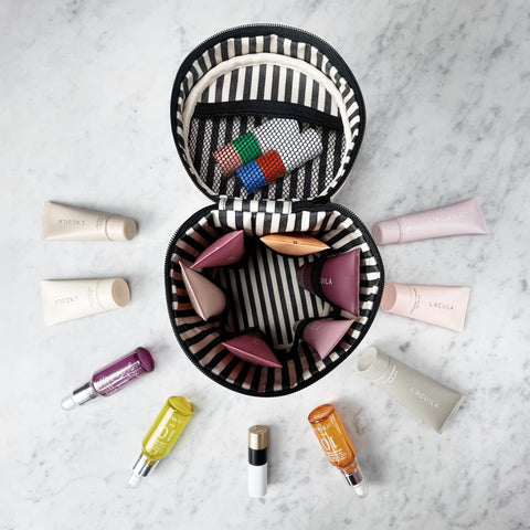 Bag-all Round My Skin Care Case in Black featuring striped interior with mesh pockets, organized compartments for skincare products, displayed open on marble surface with beauty products