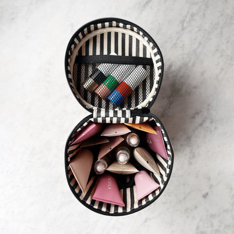 Bag-all Round My Skin Care Case in cream with striped interior, featuring organized compartments for beauty products, mesh pocket, and secure elastic bands on marble surface