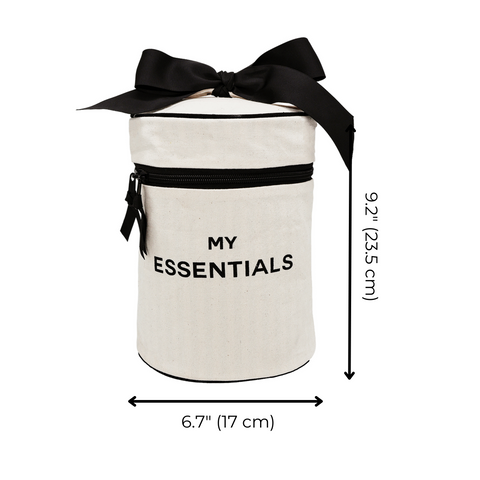 Bag-all Roomy Travel Essentials Case in cream with black bow, cylindrical shape, black zipper pocket and "MY ESSENTIALS" text. Round cotton case with waterproof lining, 9.2x6.7 inches.