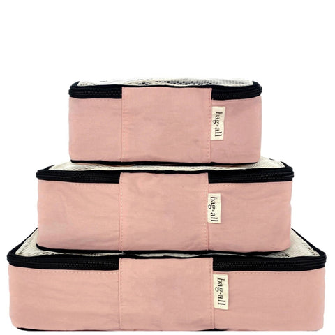 Three pink blush cotton packing cubes stacked with black zippers and mesh tops for travel organization
