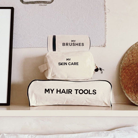 Bag-all Pamper Gift Set Deal 3-Pack Cream: Stylish cotton organizer bags for hair tools, brushes, and skincare, stacked neatly on white shelf. Natural canvas with black text labels.