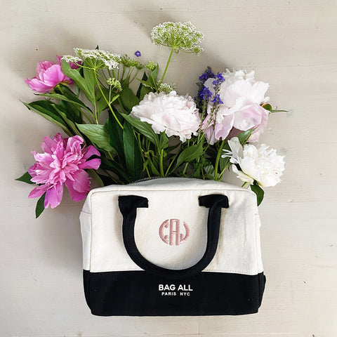Bag-all Stylish Monogram Lunch Box in cream and black with dual handles, featuring a custom monogram, shown with decorative pink peonies, white flowers and delicate Queen Anne's lace arranged inside