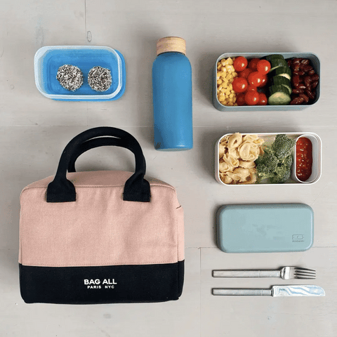 Bag-all Stylish Monogram Lunch Box in pink/blush with black trim, shown with healthy meal prep containers, reusable water bottle, and utensils for sustainable dining on-the-go