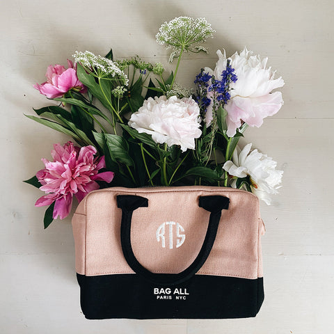 Bag-all Stylish Monogram Lunch Box in blush pink and black with monogram detail, filled with fresh spring flowers including peonies, delphiniums and Queen Anne's lace against a light background